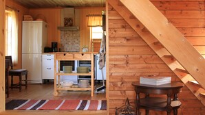 Un intérieur en bois comprenant un coin cuisine, avec un réfrigérateur, des étagères remplies de vaisselle et une table avec des livres.