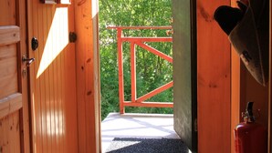 Un intérieur en bois avec une porte donnant sur un espace extérieur doté d’une rambarde rouge.