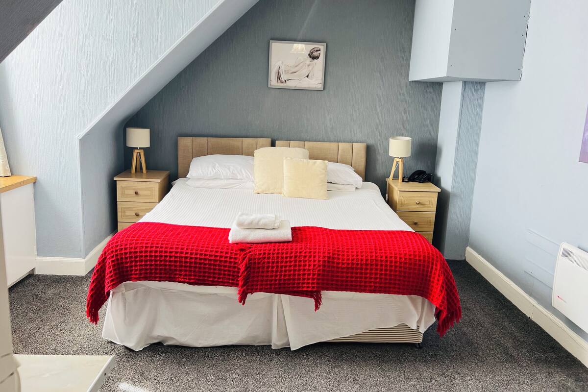 Un dormitorio ordenado con cama, dos mesitas de noche, una lámpara y un cuadro en la pared.