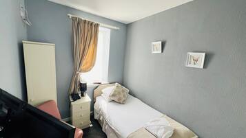 Ett hotellrum med en säng, ett sängbord, en stol, en garderob och ett fönster med gardiner.