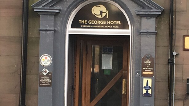 The entrance to The George Hotel with a classic arched doorway, a plaque indicating it is a round table hotel, and a sign for the Rotary Club. - Homesly The George Hotel (Montrose)
