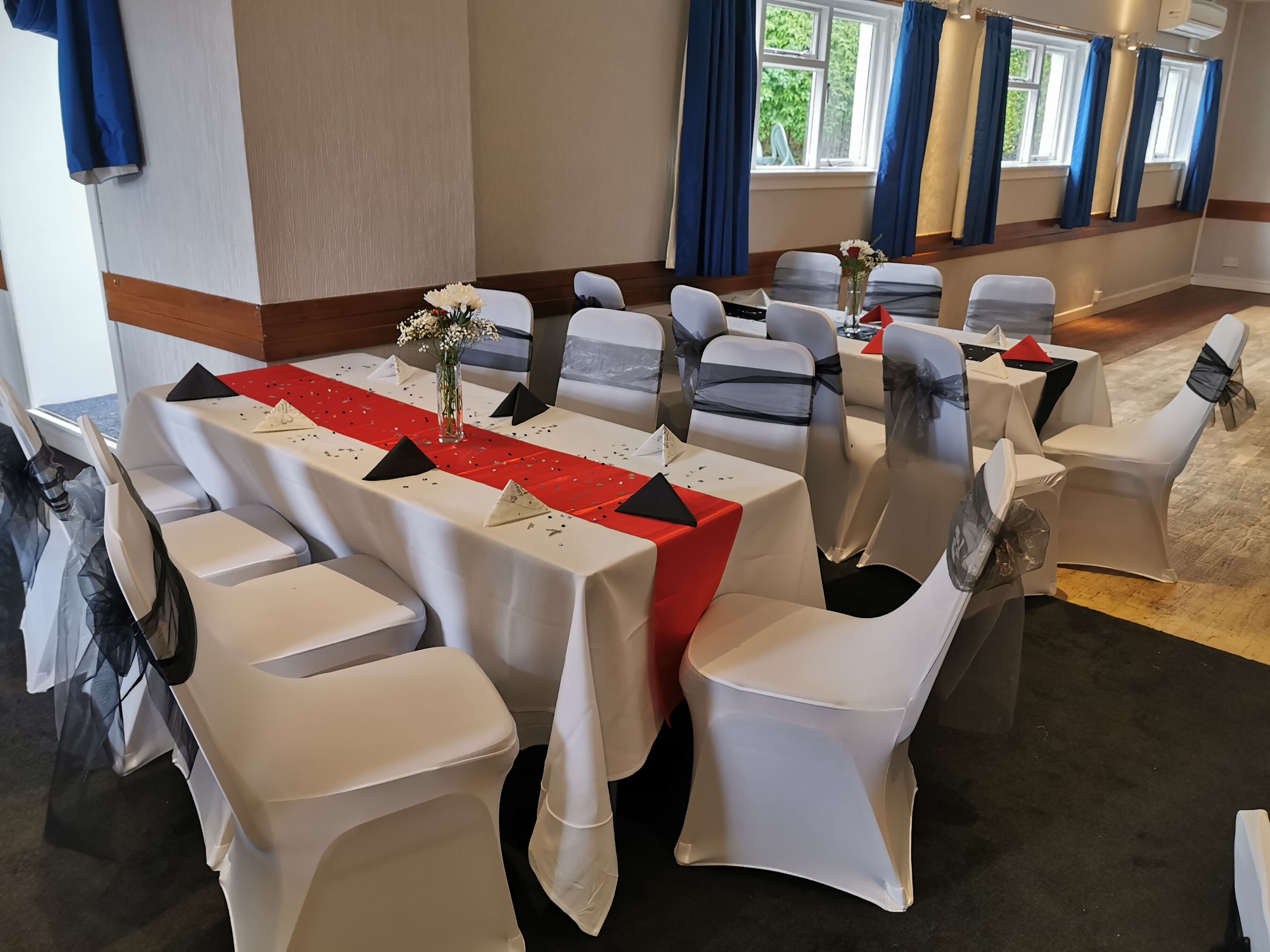 A conference room with white chairs, tables with red and black tablecloths, and blue curtains.