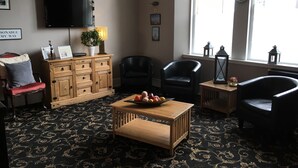 A living room with a flat-screen TV, wooden furniture, a patterned carpet, and a window with a view. - Homesly The George Hotel (Montrose)