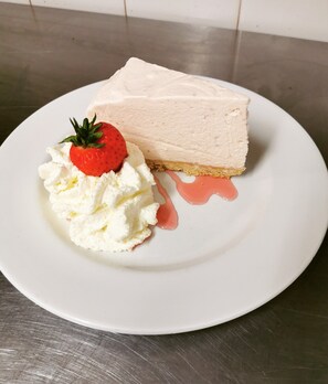 A slice of cheesecake with whipped cream and a strawberry on a white plate. - Homesly The George Hotel (Montrose)