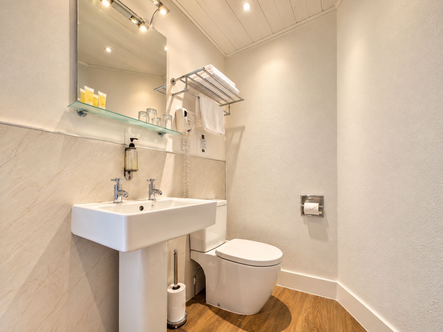 Un bagno moderno con un lavandino, un water e uno scaffale in vetro sopra il lavandino.