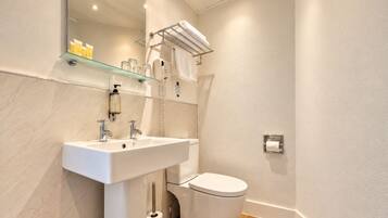 Un baño moderno con lavamanos, inodoro y estante de vidrio sobre el lavamanos.