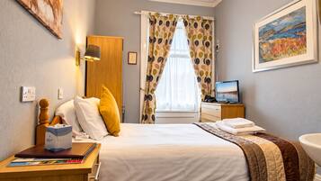 Una habitación de hotel con una cama, un escritorio con lámpara, un televisor y un cuadro en la pared.