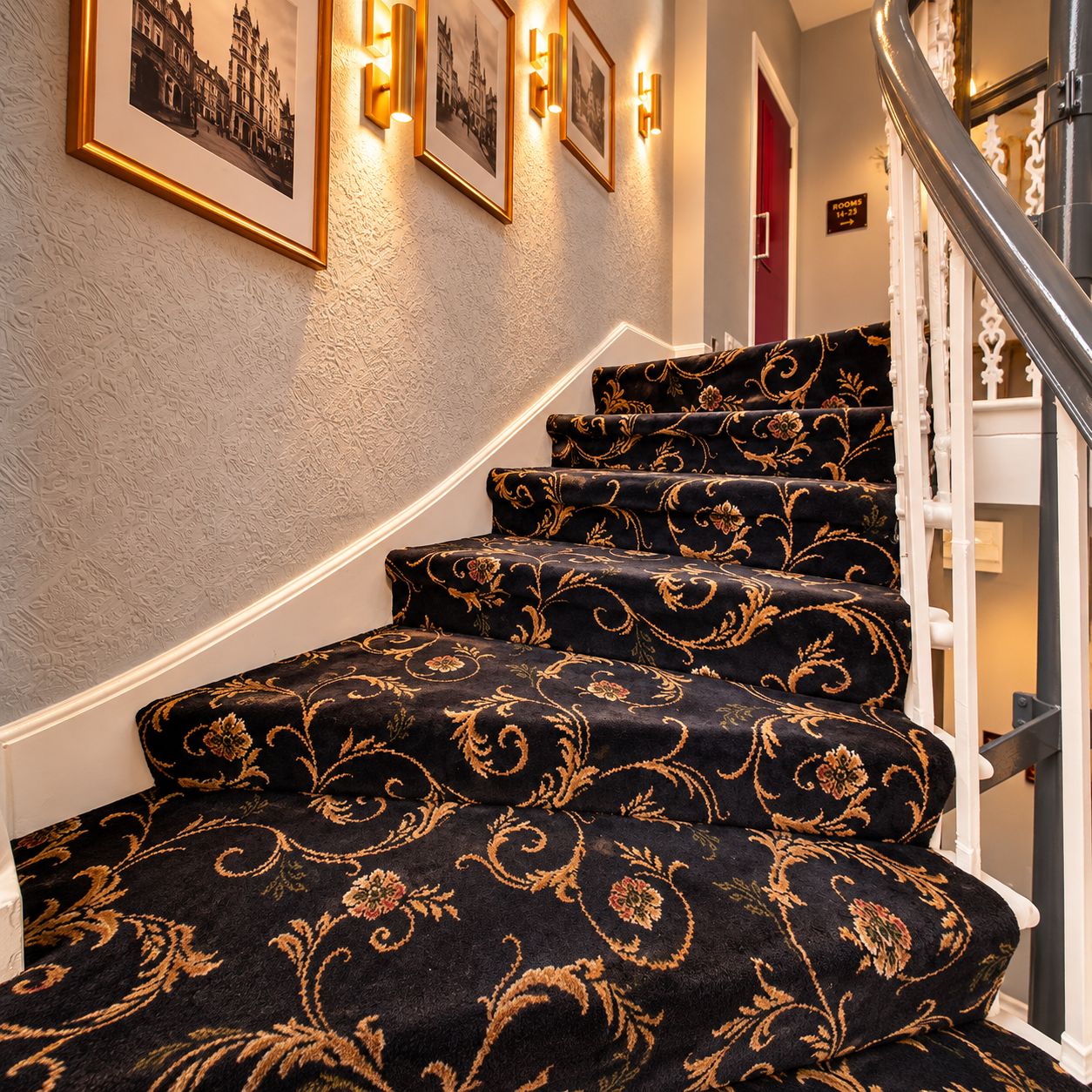 A staircase with ornate carpet patterns and wall-mounted lighting.