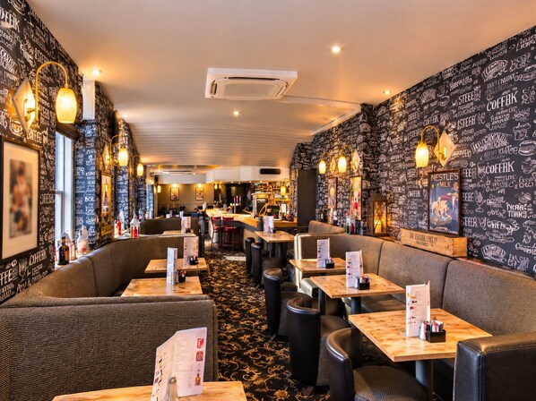 A restaurant interior with booths and tables, a patterned wall, and a bar area.