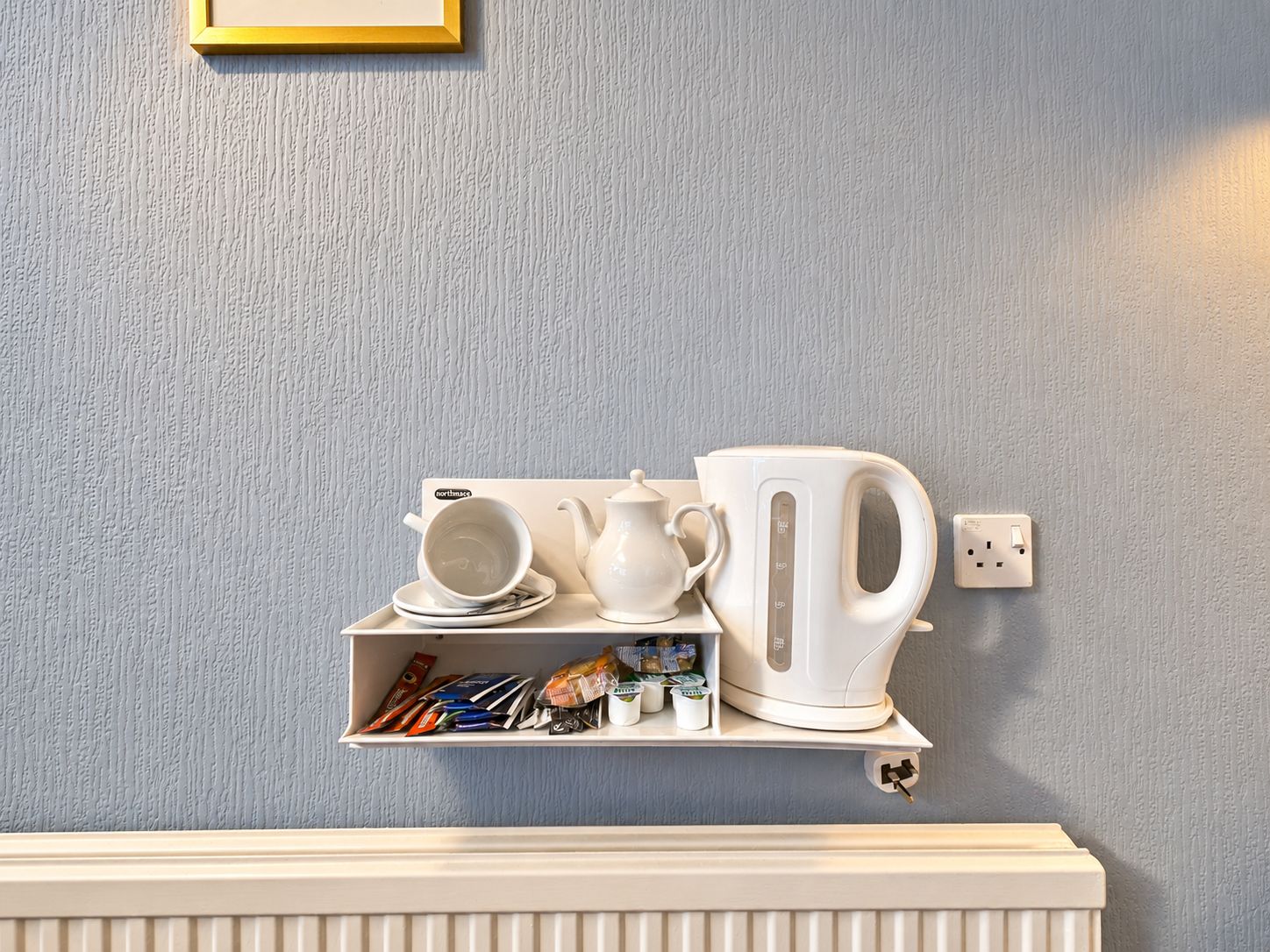 A white shelf with a kettle, a cup, and a teapot against a textured wall.