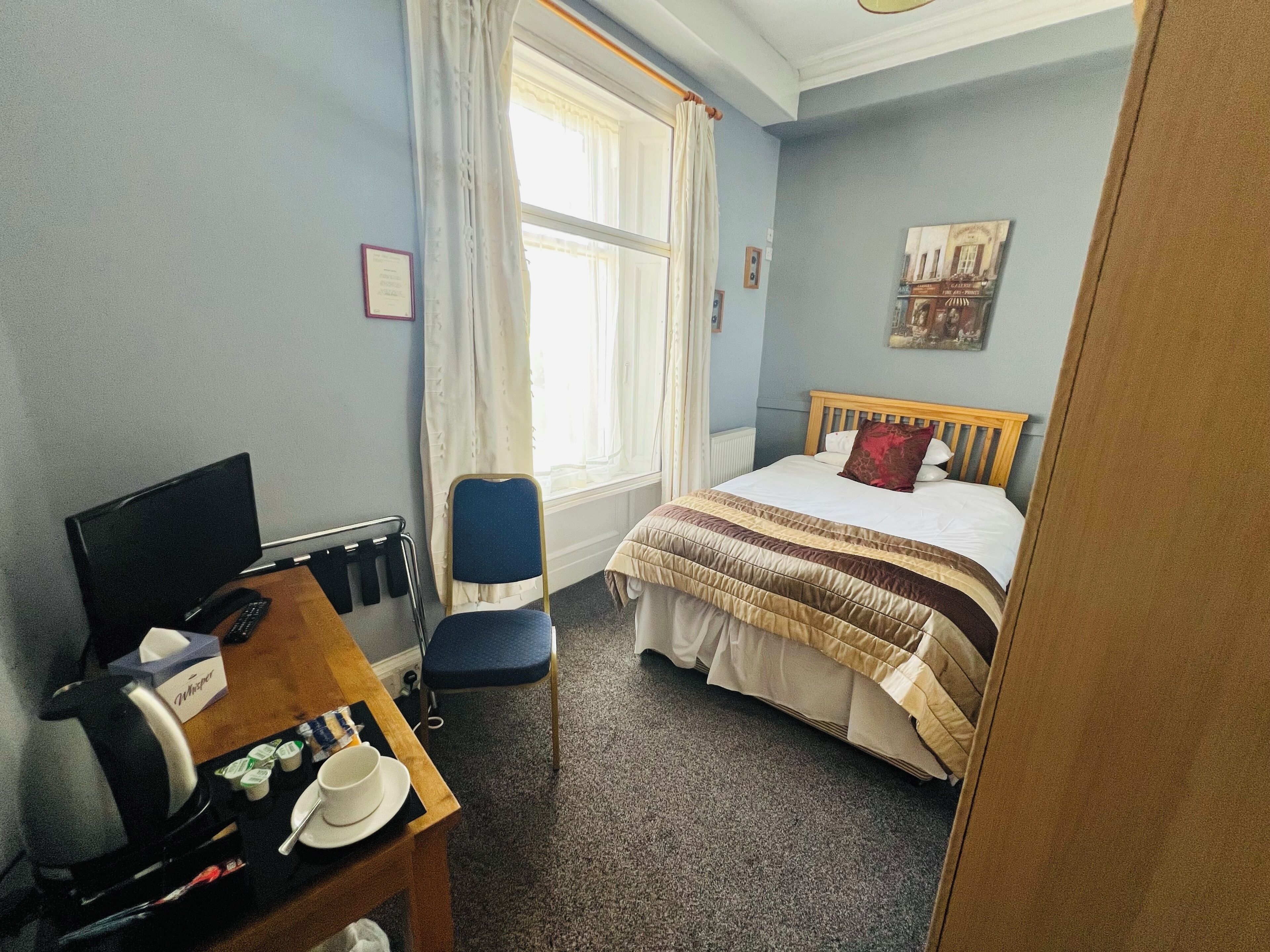Une chambre d’hôtel avec un lit, un bureau avec un ordinateur, une chaise et une fenêtre avec des rideaux.
