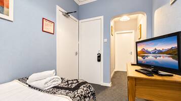 A hotel room with a bed, a television on a wooden table, a fire notice on the wall, and a door leading to another room.