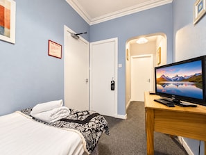 Una habitación de hotel con una cama, un televisor sobre una mesita de madera, un cartel de prevención contra incendios en la pared y una puerta que da a otra habitación.