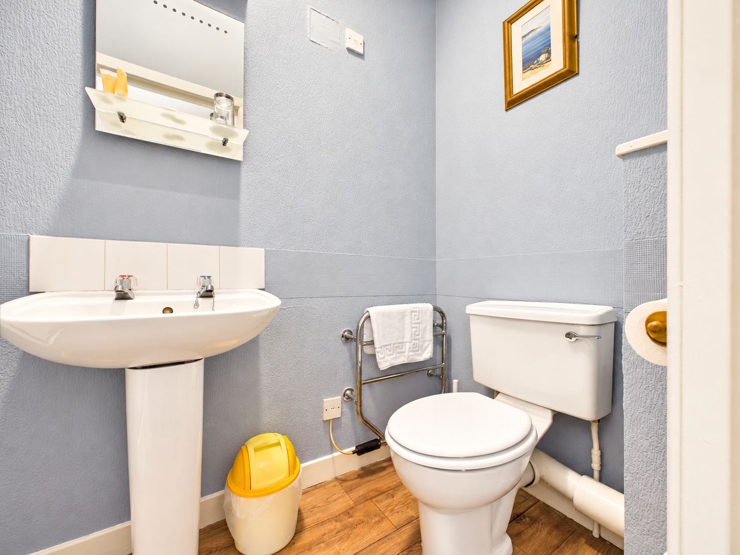 A bathroom with a white sink, toilet, and a yellow trash bin.