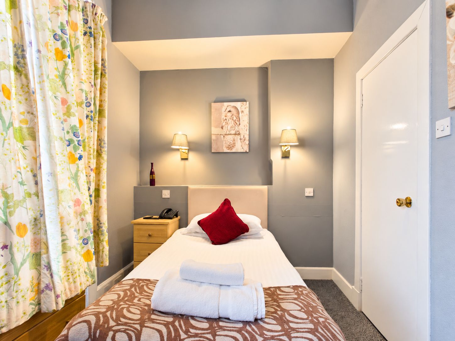 A hotel room with a bed, a nightstand, a lamp, and a door.