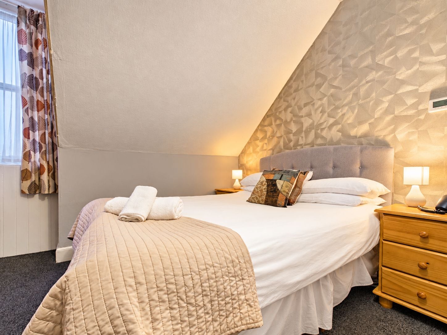 A bedroom with a bed, bedside tables, a lamp, and a patterned wall.