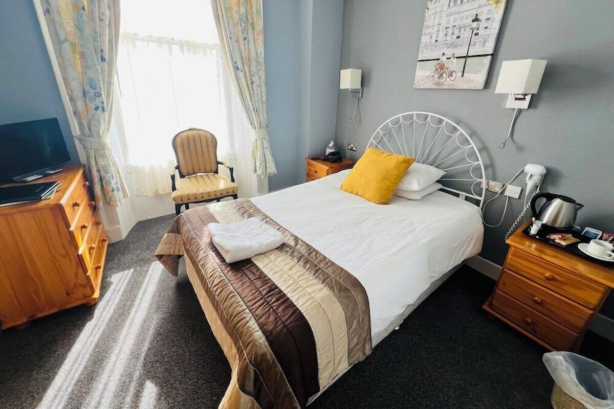 Una habitación de hotel con cama, sillón, escritorio, televisor y un cuadro en la pared.