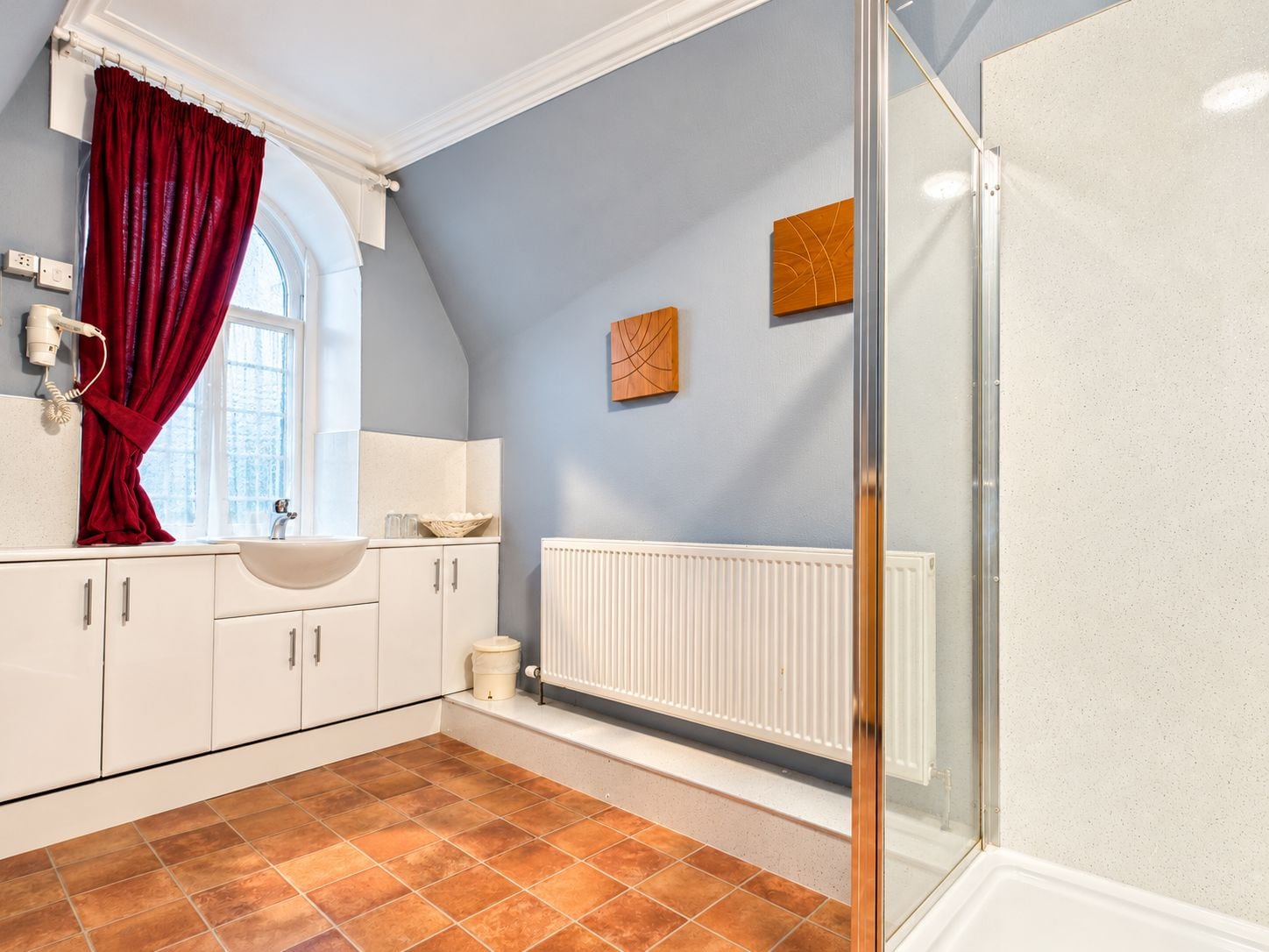 A bathroom with a white sink, a red curtain, a white radiator, and a window.