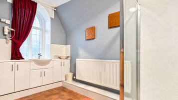 A bathroom with a white sink, a red curtain, a white radiator, and a window.
