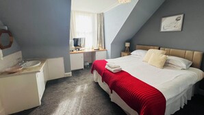 A bedroom with a bed, a desk, a chair, a nightstand, a lamp, and a window with curtains. - Homesly The George Hotel (Montrose)