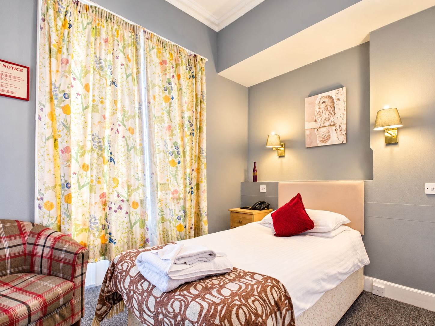 A hotel room with a bed, a chair, a bedside table, and a lamp.