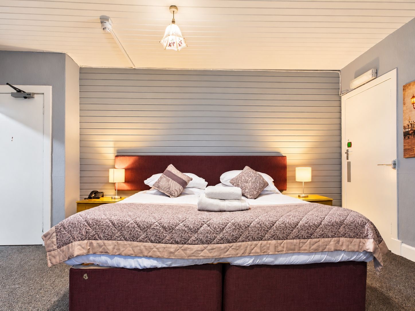 Habitación de hotel con cama, lámparas de noche, teléfono y apliques de pared.