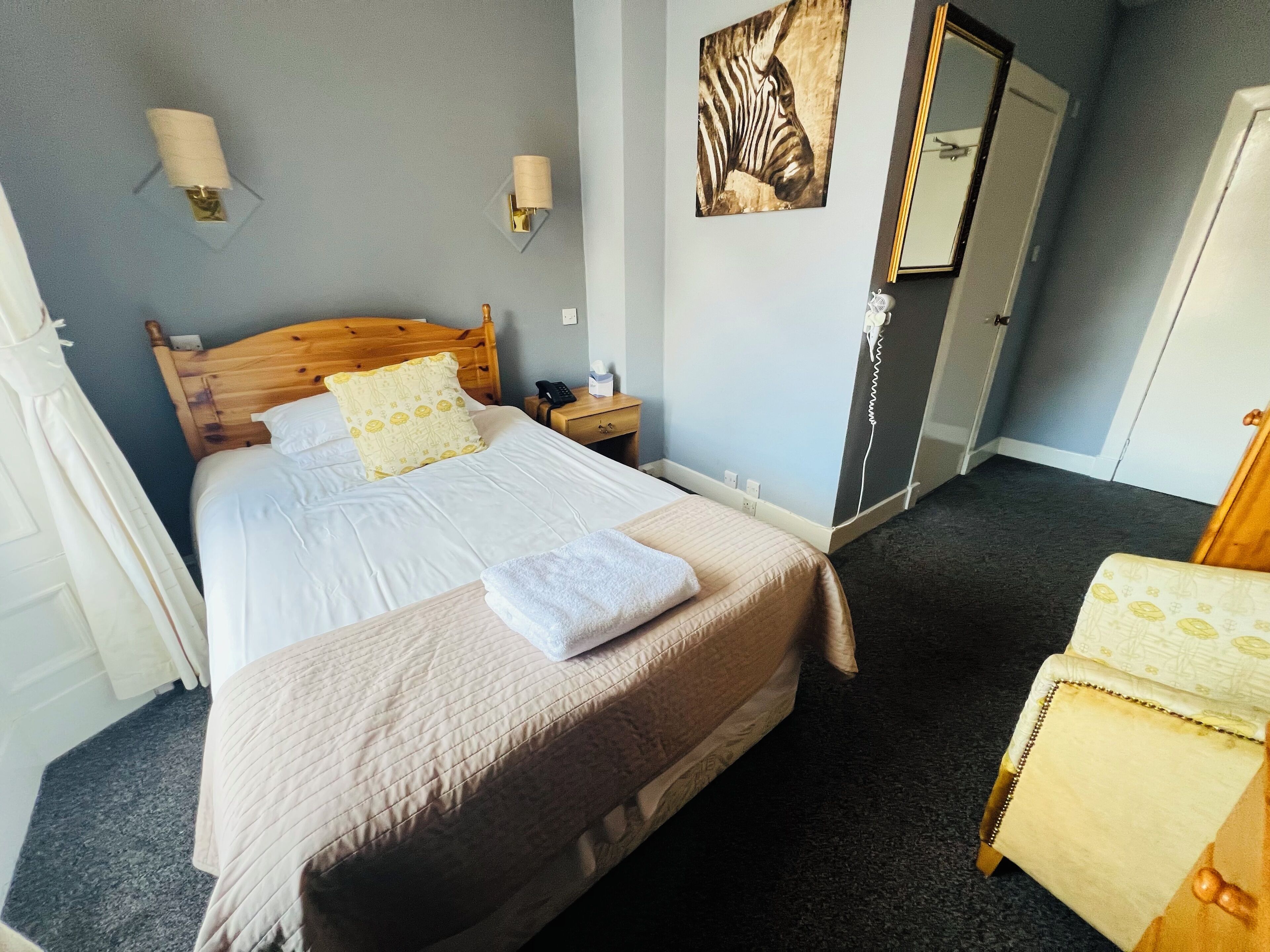 A neatly made bed with a wooden headboard, a bedside table with a lamp, and a zebra painting on the wall.