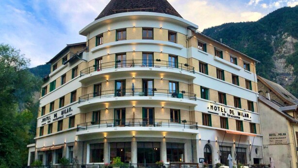 Un hôtel à plusieurs étages, doté d’une façade incurvée, de balcons et d’une enseigne bien visible indiquant « HÔTEL DE MILAN ».