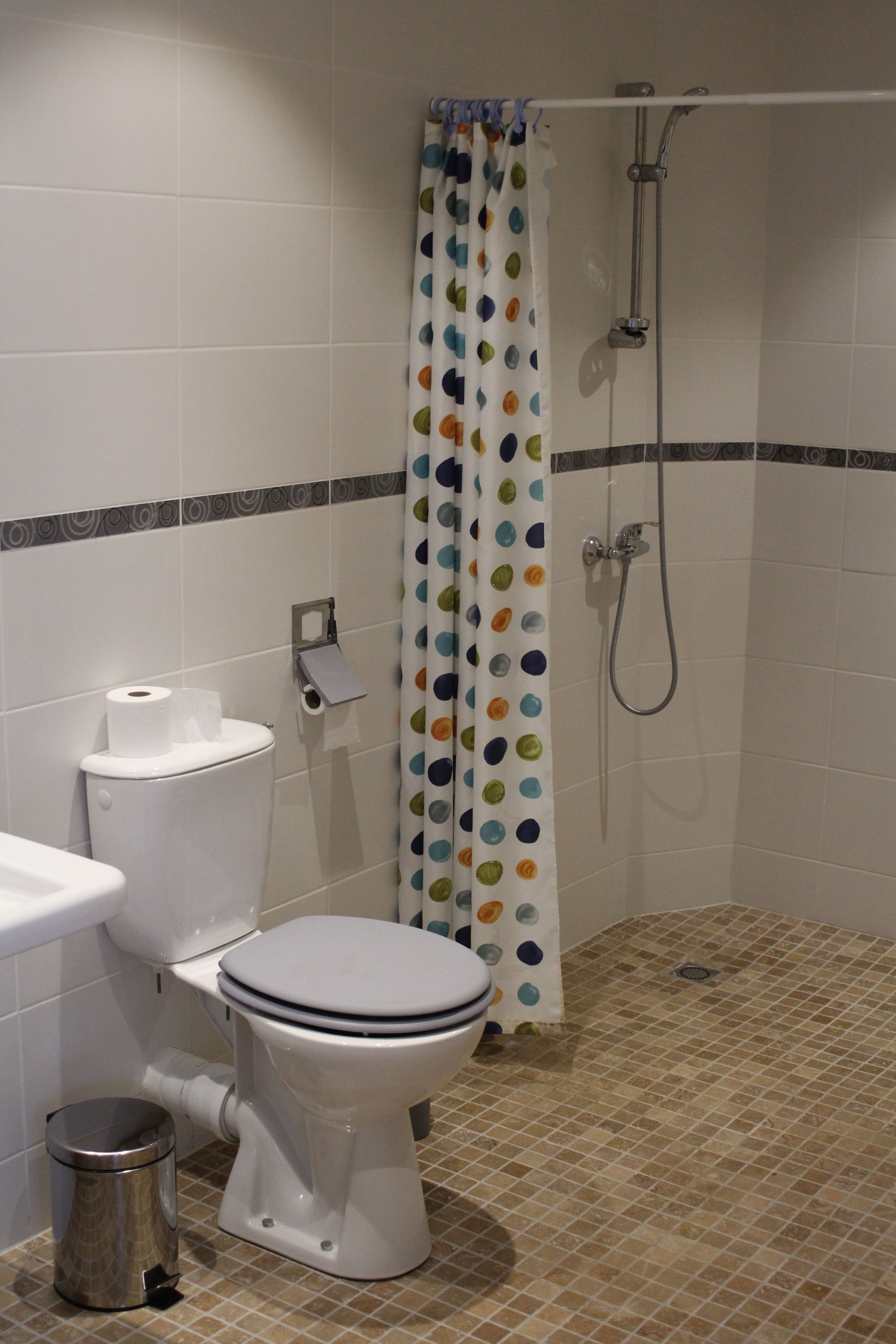 A bathroom with a toilet, a bidet, a shower, and a polka dot curtain.
