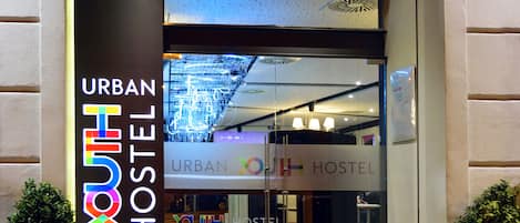 The entrance to an Urban Youth Hostel with a modern design, featuring a glass facade and a welcoming entrance.