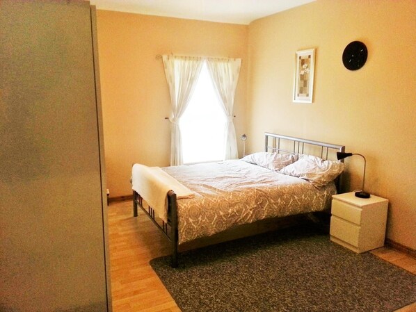 A bedroom with a bed, a bedside table, a lamp, a window with curtains, and a wall clock. - Burleigh House (Carrickfergus)