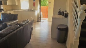 A modern kitchen with a built-in island, a dining area with a black leather couch, and a trash can.