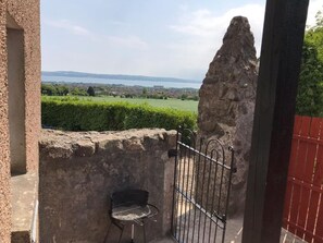 A stone wall with a metal gate and a chair, overlooking a green landscape and a distant body of water. - Burleigh House (Carrickfergus)