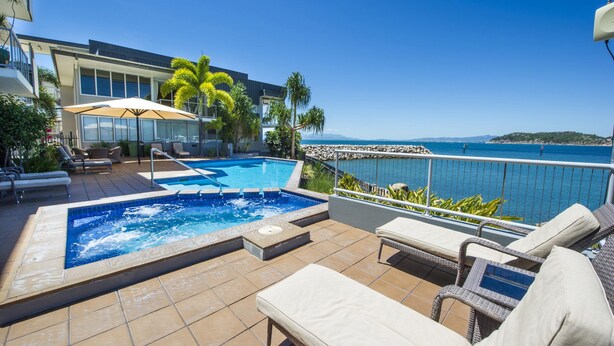 A rooftop pool area with a view of the sea, lounge chairs, and a dining area with umbrellas. - 1 Bright Point Apartment 2305 (Nelly Bay)