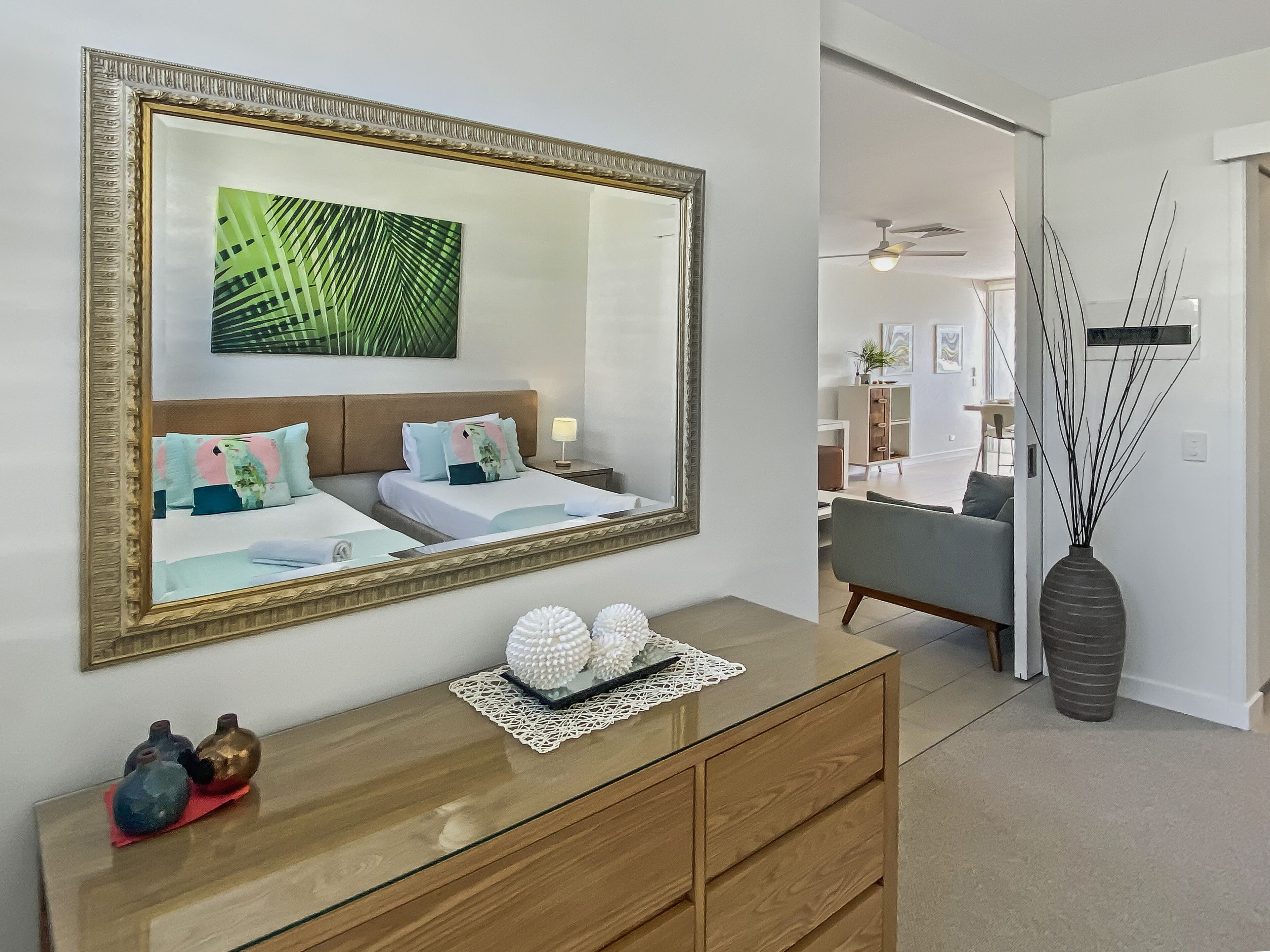 A bedroom with a large mirror, a bed with multiple pillows, a bedside table with a lamp, and a decorative vase.