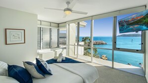A bedroom with a large bed, a ceiling fan, a view of the ocean, and a balcony with a view of the ocean. - 1 Bright Point Apartment 2305 (Nelly Bay)
