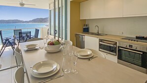 A modern kitchen with a view of the sea, a dining area with a table set for four, and a large oven. - 1 Bright Point Apartment 2305 (Nelly Bay)