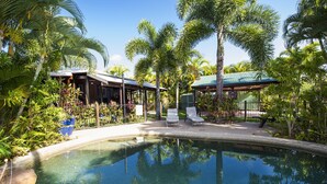 A pool surrounded by palm trees and a covered seating area with lounge chairs. - Magnetic Cottage (Horseshoe Bay)