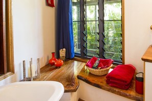 A bathroom with a wooden vanity, a white sink, a red towel, and a window with a view of greenery. - Magnetic Cottage (Horseshoe Bay)