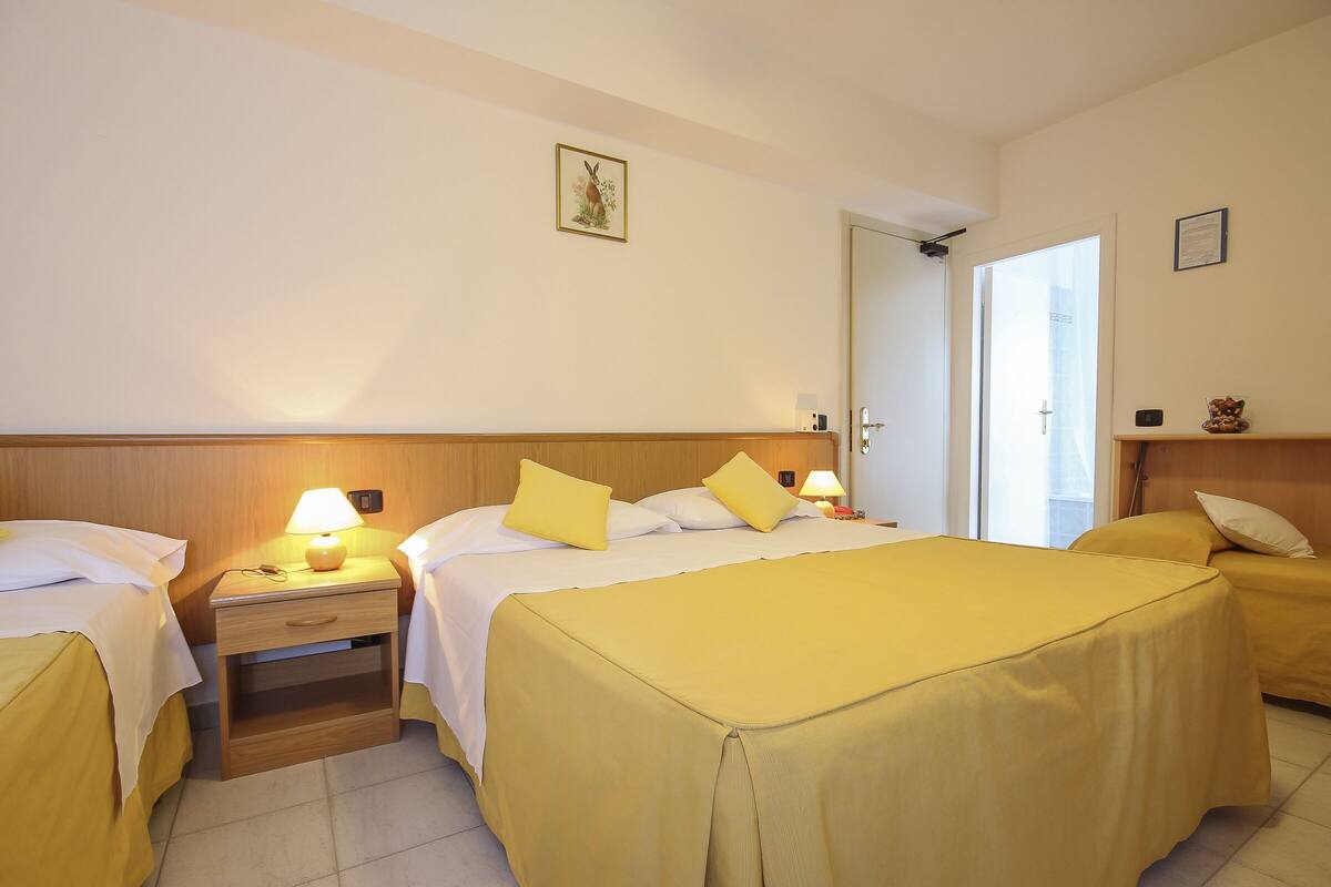 A hotel room with two beds, a nightstand with a lamp, a wooden headboard, and a door leading to a balcony.