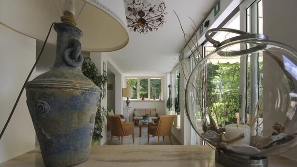 A room with a large vase, a glass dome with a decorative item inside, and a view of a dining area with a table and chairs. - Hotel Miramare (Forte dei Marmi)
