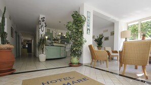 A hotel lobby with a doormat reading "HOTEL MIRAMARE," a reception desk, a dining area with wicker chairs, and a large potted plant. - Hotel Miramare (Forte dei Marmi)