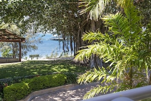 Guests can relax under the shade of a pergola, surrounded by a well-maintained garden with a serene view of the water.