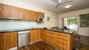 A modern kitchen with wooden cabinets, a dishwasher, and a microwave. - Picnic Bay Apartments Unit 3 (Picnic Bay)