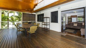 A spacious room with a wooden deck, a dining area with a table and chairs, and a living area with a sofa and a coffee table. - Picnic Bay Apartments Unit 3 (Picnic Bay)