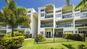 A multi-story hotel with balconies, a well-maintained lawn, and tropical plants. - Beachside Apartment 14 (Nelly Bay)