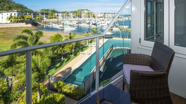 A balcony with a view of a marina, a swimming pool, and a building with a white facade. - Beachside Apartment 14 (Nelly Bay)