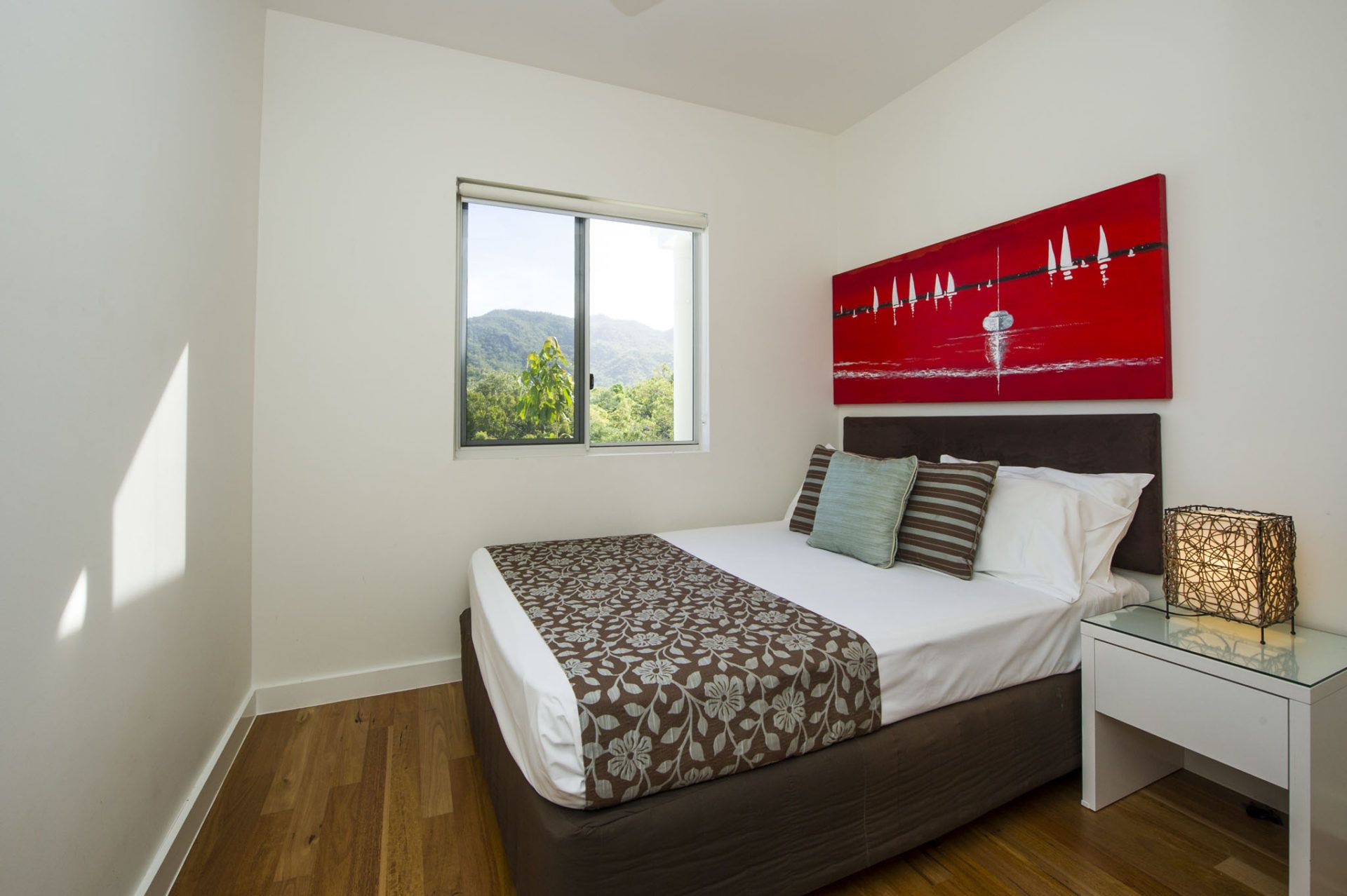 A bedroom with a bed, a nightstand, a lamp, and a painting of sailboats.