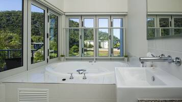 A modern bathroom with a large bathtub, a separate sink, and a large window offering a view of greenery and buildings.