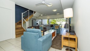 A modern living room with a staircase, a dining area, and a kitchen. - Beachside Apartment 13 (Nelly Bay)
